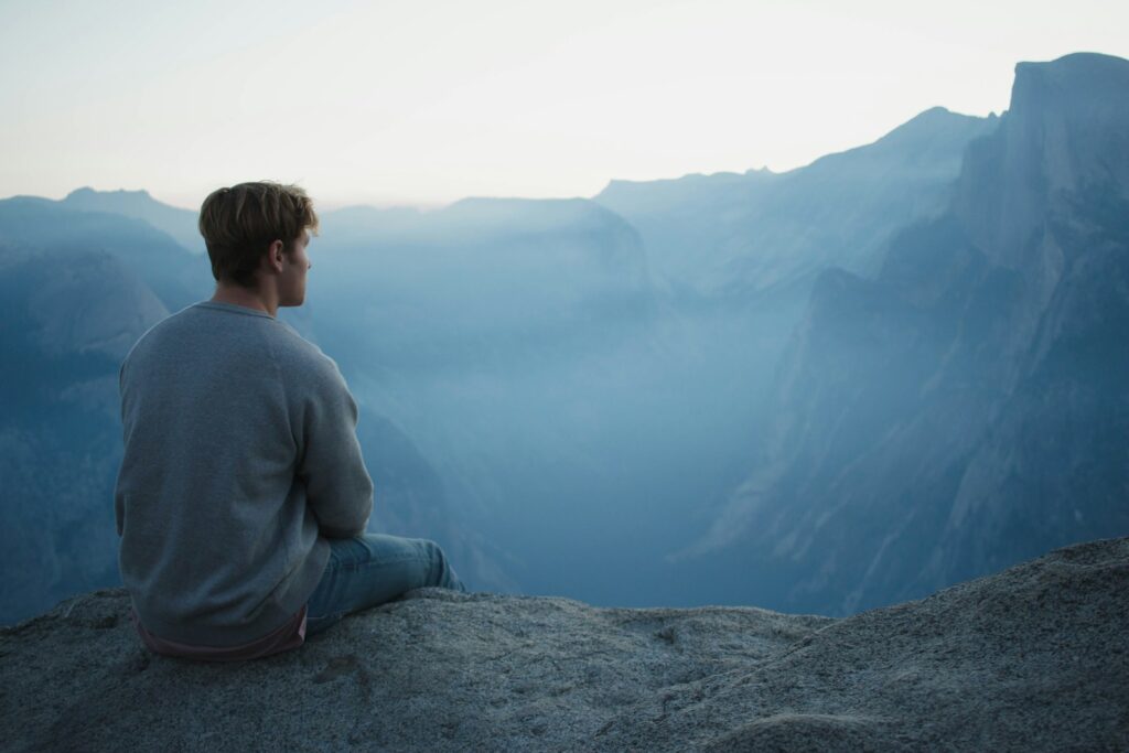 man in gray shirt sits on cliff - a picture that I choose to talk about how do I deal with stress at work with Stoicism. 