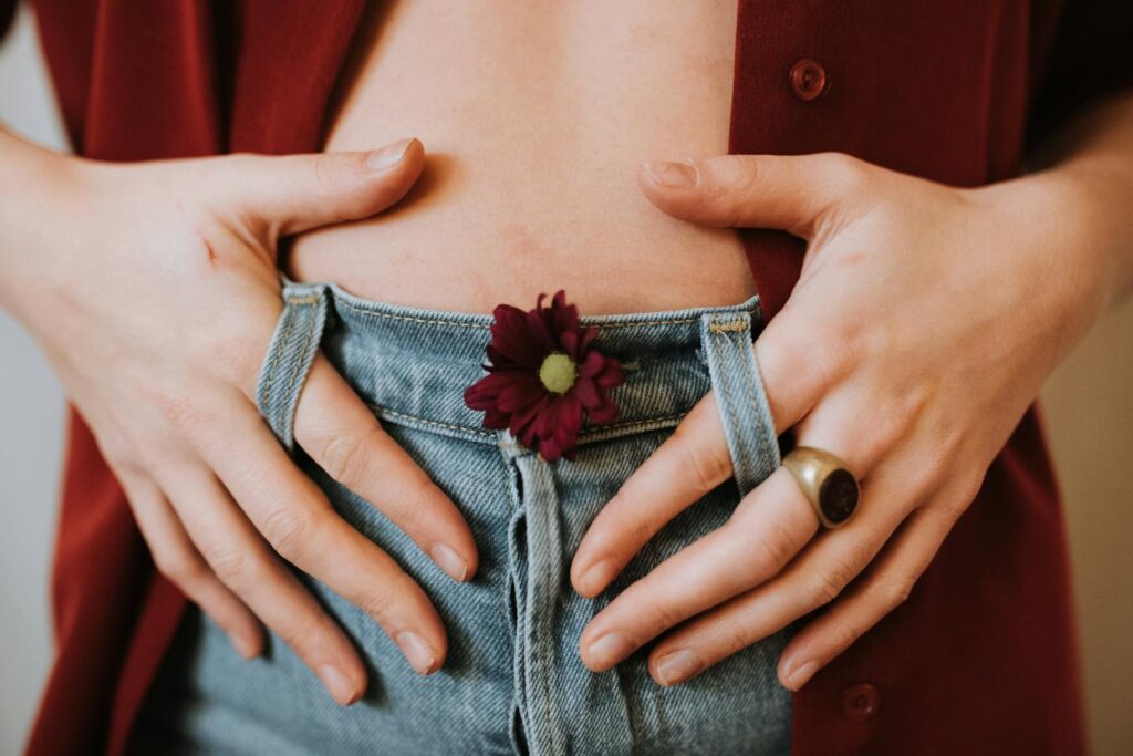Crop faceless female in casual clothes decorated with blooming flower revealing bare stomach