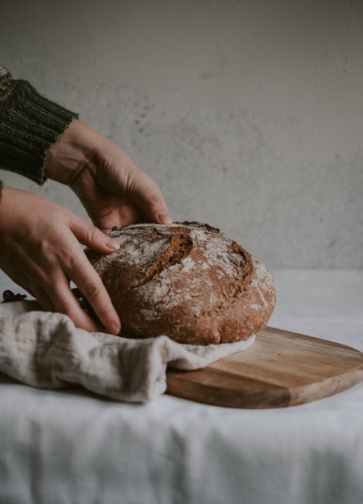 person holding brown bread on brown wooden chopping board - and this picture is use to answer this question: Is sourdough good for gut health?